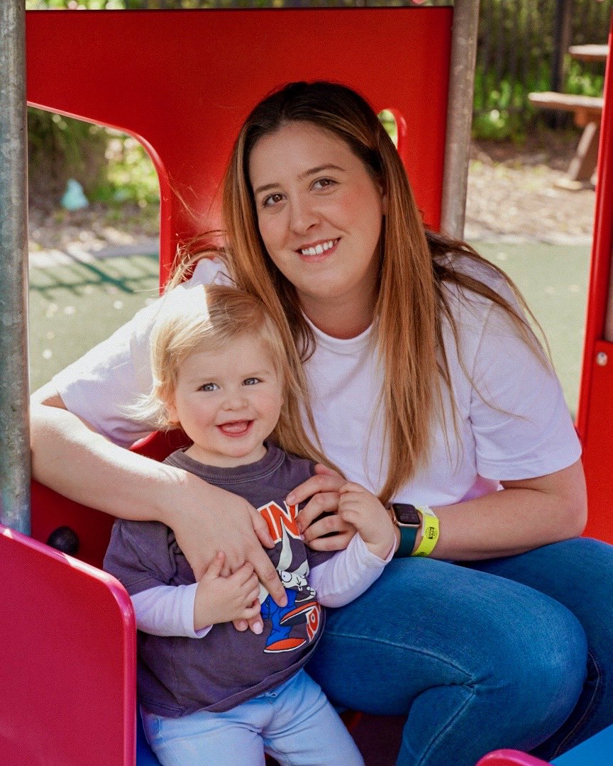 Amy King smiling in a playground with a little one on her lap