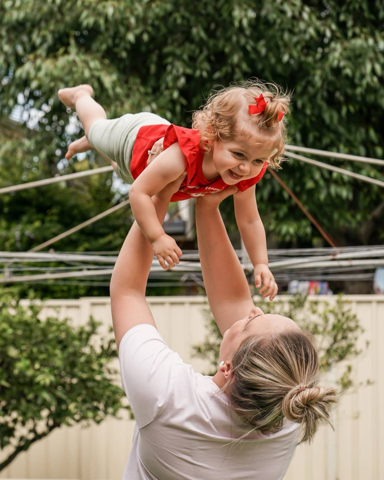 Mum lifting her laughing toddler high into the air in the backyard